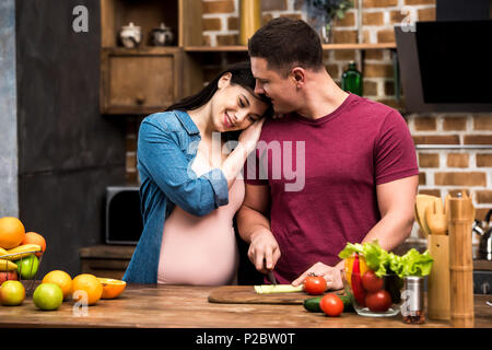 Glückliche junge schwangere Paare stehen zusammen, beim Kochen in der Küche Stockfoto