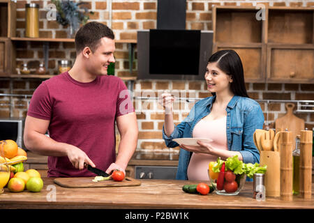 Glückliche junge schwangere Paar lächelnd während sie zusammen kochen Stockfoto