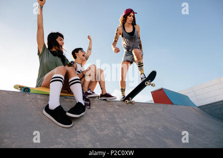 Drei junge weibliche Freunde am Skatepark. Skater girl ihre Routine mit Frauen Freunde jubeln sitzen auf der Rampe. Stockfoto