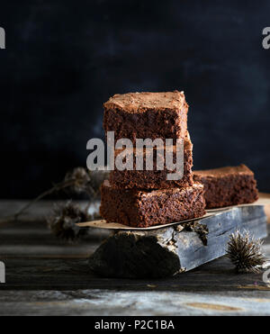 Ein Stapel von quadratische Stücke von gebackenen Braun brownie Torte auf einem grauen Board, ein schwarzer Hintergrund Stockfoto