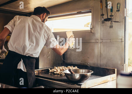 Junge Küchenchef kochen einige seiner bevorzugten Gerichte in Essen Lkw. Mann Vorbereitung Essen auf Herd in seinem Essen. Stockfoto