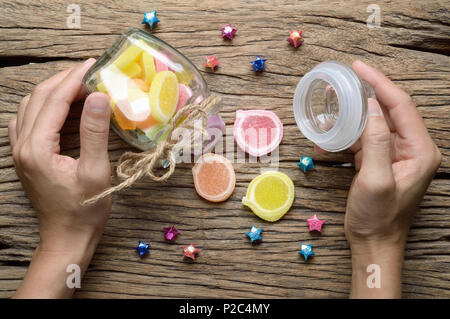 Blick von oben auf die Frau Hand offen Glas Flasche jelly candy Dessert auf Holz- Hintergrund Stockfoto