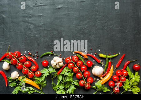 Hot Chili peppers Mehrfarbige, Tomate Kirsche auf Zweig, Knoblauch und andere Gewürze auf schwarzem Hintergrund Kopie Raum. Stockfoto
