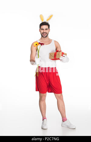 Lächelnder Mann mit Hasenohren mit Blumen und Geschenk Box auf Weiß, Ostern Konzept isoliert Stockfoto