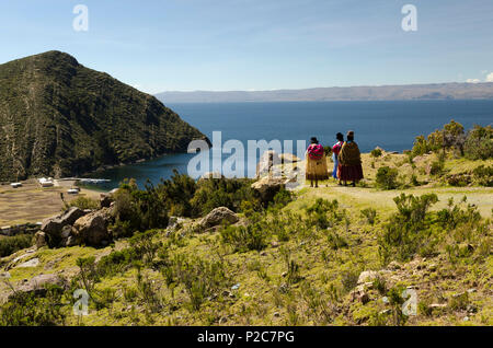 Drei cholitas, einheimische Frauen in traditioneller Kleidung, auf einem Pfad auf der Insel Isla del Sol, im Hintergrund Titicaca See, Stockfoto