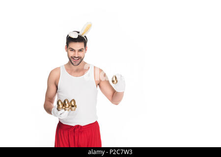 Lächelnder Mann mit Hasenohren und goldene Eier auf Weiß, Ostern Konzept isoliert Stockfoto