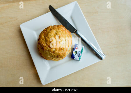 Einen frisch gebackenen Käse scone mit einem Messer und einer einzelnen Teil der gewickelten Butter auf einem weißen Teller Stockfoto
