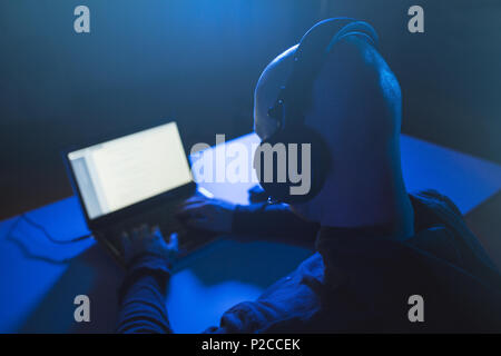Hacker mit Headset Tippen auf Laptop im dunklen Zimmer Stockfoto