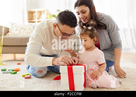 Baby Mädchen mit Geburtstagsgeschenk und Eltern zu Hause Stockfoto