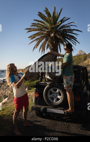 Männliche Freunde Surfboard entfernen, die von dem Jeep Stockfoto