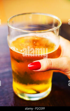 Hand von einer Frau mit einem Glas 500 ml Bier ohne Schaum auf einem holztisch an einem sonnigen Tag. Stockfoto