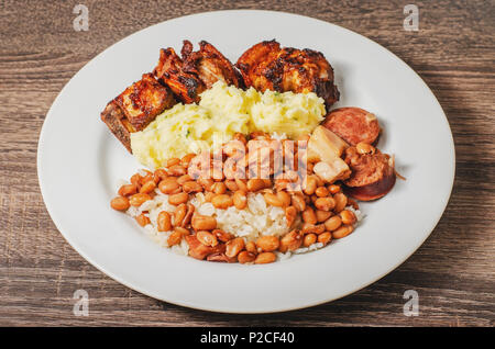 Brasilianische Küche, Teller mit Reis und Bohnen (arroz com feijao) gewürzt mit Wurst und Speck, Kartoffelpüree und Schweinefleisch (costelinha de Porco). Weiß Stockfoto