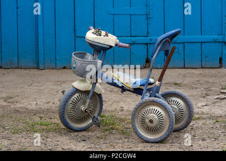 Gebrochene Kinder Fahrrad auf dem Hintergrund der blauen Türen aus Holz Stockfoto