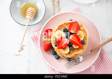 Stapel von hausgemachte Pfannkuchen mit Erdbeeren, Banane und Brombeeren auf einem rosa Platte. Ansicht von oben Stockfoto