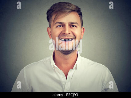 Portrait von gutaussehenden jungen Mann im weißen T-Shirt positiv an Kamera lachend auf grauem Hintergrund Stockfoto