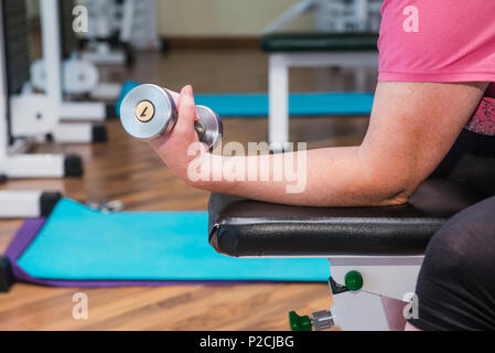 Schließen Sie kein Gesicht senior Frau aktiv spezielle Übungen, Arbeit mit Gewichten in der Turnhalle am Krankenhaus Rehabilitation Centre. Selektiver Fokus, Platz für Text. Stockfoto