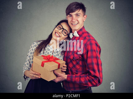 Junge Inhalt Paar umarmen und stehend mit Geschenkbox in Feier und Kamera Stockfoto