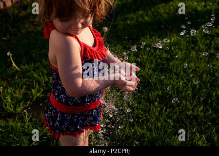 Ein junges Mädchen spielt in Wasser aus einem Schlauch während des Sommers. Stockfoto