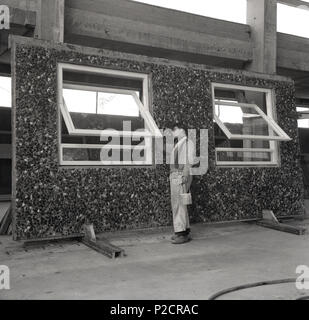 1960, historische, einem Arbeiter, der Malerei die die Holzfenster auf einem Kiesel - Dash abgedeckt Betonfertigteile frame, England, UK. Während dieser Zeit, viele neue 'modernen' Bürogebäude und Hochhaus Wohnungsbau verwendet ein Produkt mit Fenster- und Türöffnungen bereits in die Wände werfen bei der Fertigungsanlage, ie Hergestellt aus Ort, mittels wiederverwendbaren Formen, die hatte mehrere Vorteile; es erlaubt constructon eines Gebäudes, schneller zu sein, Wetter unabhängig und damit den Standort Verzögerungen und Mantaining Zeitpläne. Auch Umweltbelange wie Staub und Lärm reduziert werden. Stockfoto