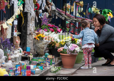 Ein kleines Kind schaut auf Blumen in der Nähe, wo die Grenfell Feuer aufgetreten ist links, am ersten Jahrestag des Hochhauses Katastrophe, am 14. Juni 2018 in London, England. 72 Menschen starben, als der Turm im Stadtteil Kensington & Chelsea, in welcher der größte Brand seit WW2 aufgerufen wurde getötet wurden. Das 24-stöckige Hochhaus Grenfell von Sozialwohnungen Wohnungen in Kensington, West London, Vereinigtes Königreich. Es verursachte 72 Todesfälle, in der 293 Personen im Gebäude, darunter 2, die Entronnenen und verstarb im Krankenhaus. Mehr als 70 wurden verletzt und traumatisiert. Ein 72-zweite nationale Stille war Hel Stockfoto