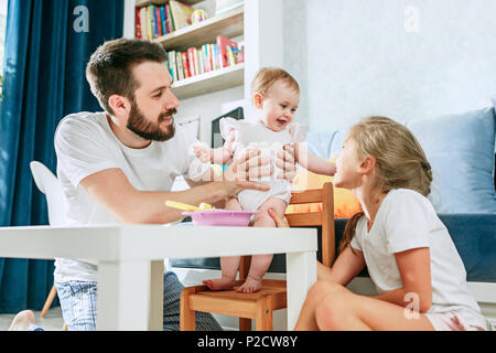 Gut aussehende junge Mann essen Frühstück und Ihr Baby füttern zu Hause Stockfoto