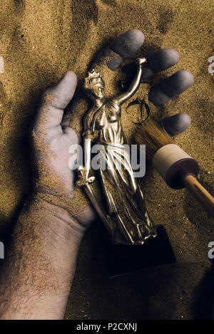 Forensische Experten entdecken Leiche in der Wüste Sand mit Gerechtigkeit Statue in der Hand begraben. Konzeptionelle Bild für die polizeiliche Untersuchung eines kalten Fall mur Stockfoto