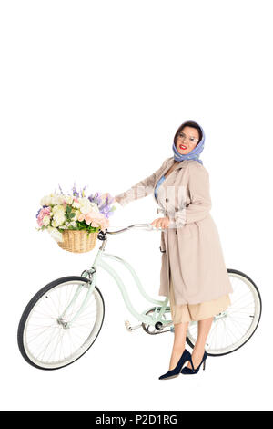 Schöne Übergrößen Frau in stilvollen Trenchcoat und Halstuch mit Vintage Fahrrad mit Blumen im Korb auf weißen isoliert Stockfoto