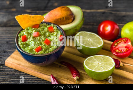 Guacamole in blauer Schüssel mit Tortilla Chips und Zitrone auf natürliche Holzschreibtisch. Stockfoto