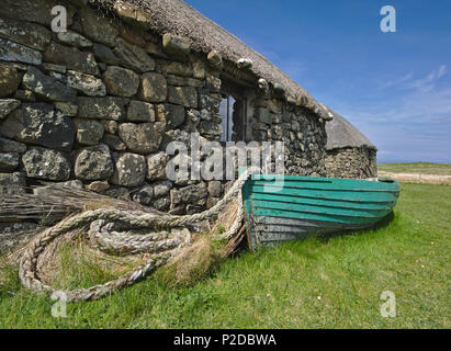 Traditionelle Hebridean blackhouse mit Strohdach, Holz- Boot und Seil aufgerollt. Stockfoto