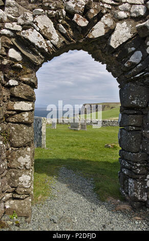 Isle of Skye, Schottland - Blick durch den Torbogen der verfallenen Trumpan Kirche über eine grüne Wiese Friedhof auf dem Weg zu einem entfernten Meer Felsen Stockfoto