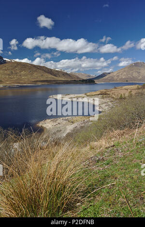 Loch Cluanie, Scottish Highlands unter einem blauen Himmel mit schneebedeckten Gipfeln im Hintergrund Stockfoto