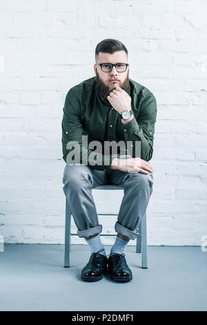 Nachdenklich stilvolle Geschäftsmann sitzen auf Stuhl gegen weiße Wand Stockfoto