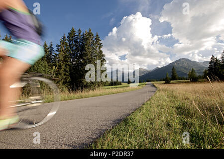 Junge Frau reiten ihr Fahrrad in der Nähe von Bergen an einem sonnigen Tag, Tannheimer Tal, Tirol, Österreich Stockfoto