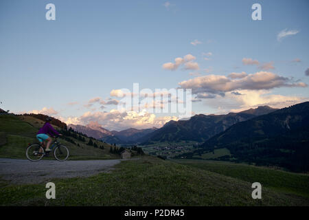 Junge Frau reiten ihr Fahrrad in der Nähe der Berge bei Sonnenuntergang, Rote Flueh, Gimpel, Hochwiesler, Tannheimer Tal, Tirol, Österreich Stockfoto