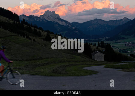 Junge Frau reiten ihr Fahrrad in der Nähe der Berge bei Sonnenuntergang, Rote Flueh, Gimpel, Hochwiesler, Tannheimer Tal, Tirol, Österreich Stockfoto