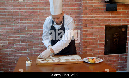 Koch schneiden Sie Kreise aus roher Plätzchenteig gerollt Naht auf einem Holzbrett Stockfoto