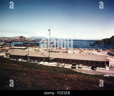 . Die US-Marine Naval Operating Base, Er, Alaska (USA): Ansicht eines Verwaltungsgebäudes, mit dem Hafen hinaus, ca. Sommer 1944. Das getarnte Schiff in der Mitte des Hafens, über die Fahnenstange, Ausschreibung ist der Zerstörer USS Black Hawk (AD-9). USS Charleston (PG-51) wird zwischen dem Pier und den Escort Ship (DE), direkt hinter der Fahnenstange. Eine "Freiheit" Schiff und andere Schiffe sind ebenfalls vorhanden. Sommer 1944. USN 36 Naval Operating Base er im Sommer 1944 (01) Stockfoto