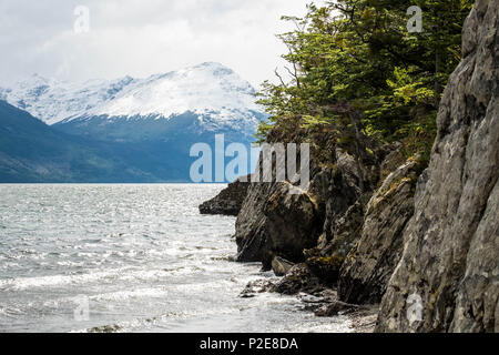 Eine Klippe grenzt an den Acigami-See im Nationalpark Feuerland, Berge sind auf der anderen Seite. Dieser See verbindet Argentinien und Chile. Stockfoto