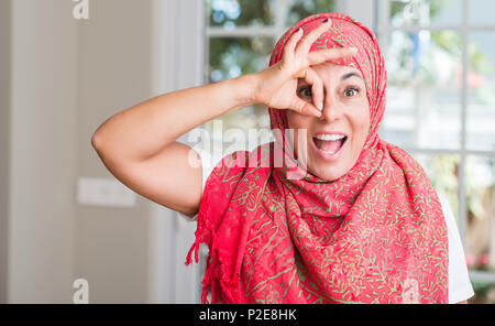 Im mittleren Alter muslimische Frau hijab tragen mit glücklichen Gesicht lächelnd tun ok Zeichen mit der Hand auf Auge schauen durch die Finger Stockfoto
