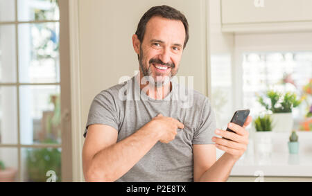Mittleres alter Mann mit Smartphone mit Überraschung Gesicht zeigenden Finger zu sich selbst Stockfoto