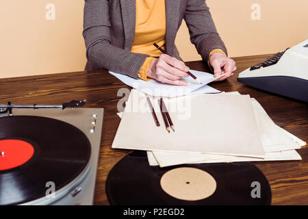 7/8 Bild der Frau schreiben in Papier am Tisch mit Schallplatten, Plattenspieler und Schreibmaschine Stockfoto