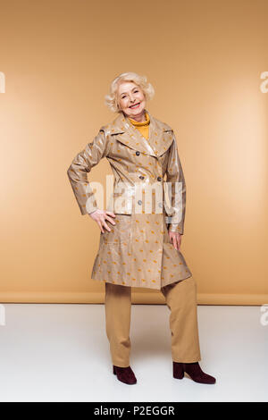 Gerne stilvolle ältere Frau im Trenchcoat posiert Stockfoto