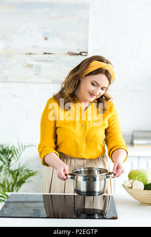 Schöne Frau setzend Topf auf Herd in der Küche Stockfoto