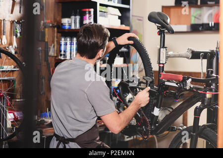 Rückansicht der jungen Arbeiter Fahrrad zur Festsetzung in der Werkstatt Stockfoto