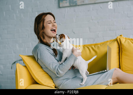 Attraktive schwangere Frau Lachen und Spielen mit Jack Russell Terrier im Wohnzimmer Stockfoto