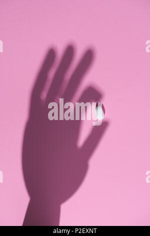 Blick von oben auf die Schatten einer Hand, die eine Pille auf rosa Oberfläche Stockfoto