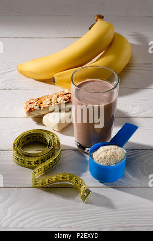 Glas Protein Shake mit Bananen und Energieriegel auf weissem Holztisch Stockfoto