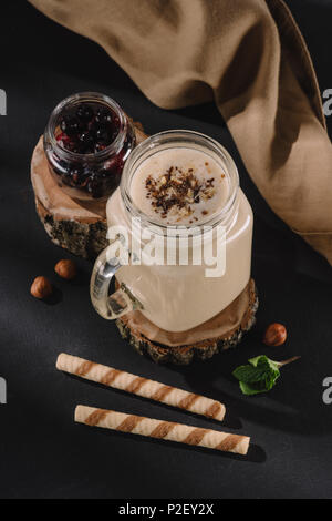 Detailansicht aus Glas mit milchshake auf hölzernen Slice, Korinthen, Walnüsse, Minze, süße Strohhalme und Küchenpapier Stockfoto
