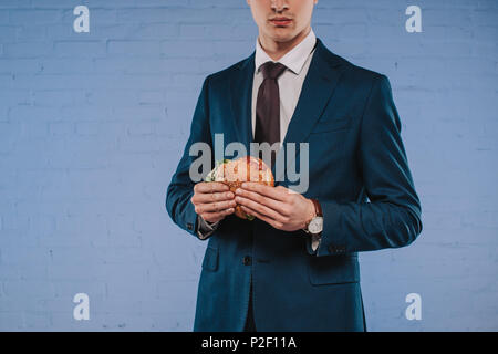 7/8 shot junger Geschäftsmann in Anzug holding Burger Stockfoto