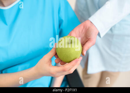 7/8 Schuß von Arzt vorbei an grünen Apfel für schwangere Frau im Rollstuhl Stockfoto